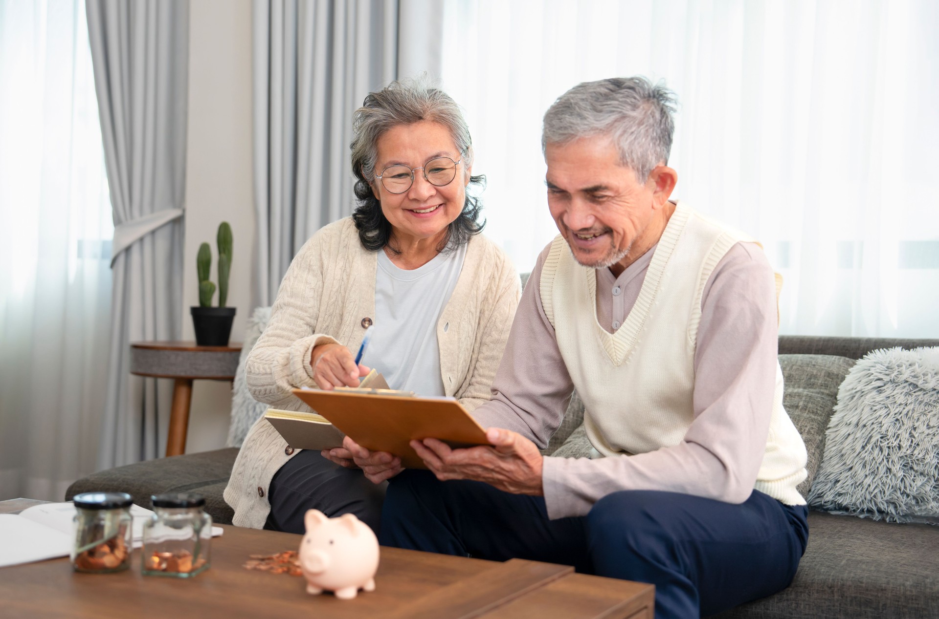 asian senior couple is looking for savings plan together,old man holding money savings chart,his wife holding note book,they are smiling happily